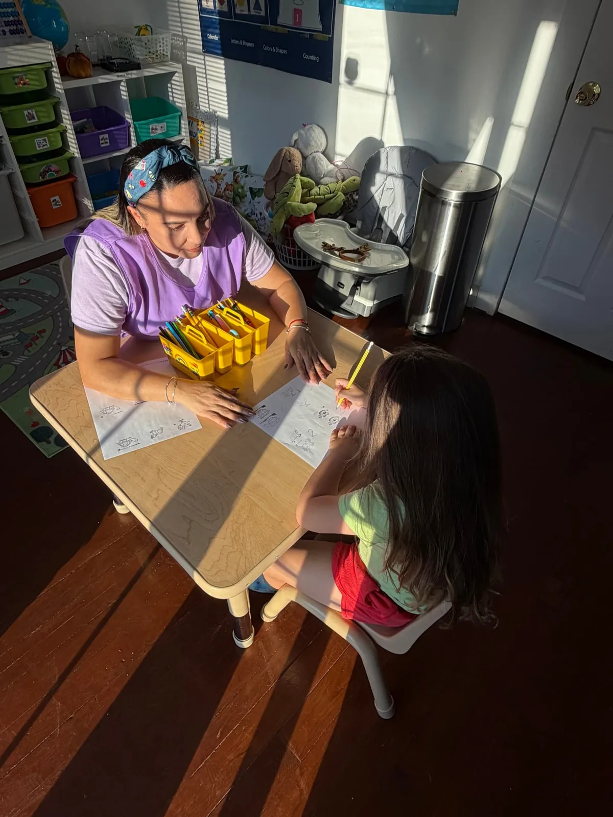 The daycare owner supporting a child as they work on a worksheet together.